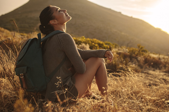 Woman sitting in field embracing the last of the days sun whilst hiking
