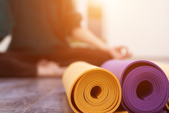 Close up of yellow and purple yoga mats with yogi practicing in background